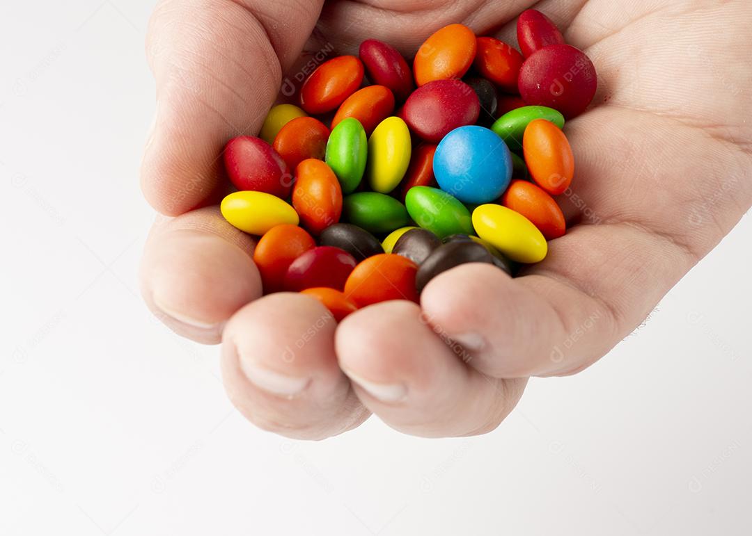 Hand holding colorful candies on white background.