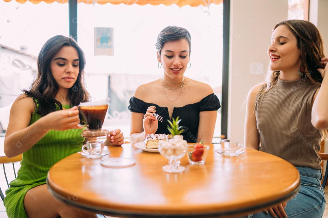 Young latin girls sitting in cafe drinking coffee and eating cake