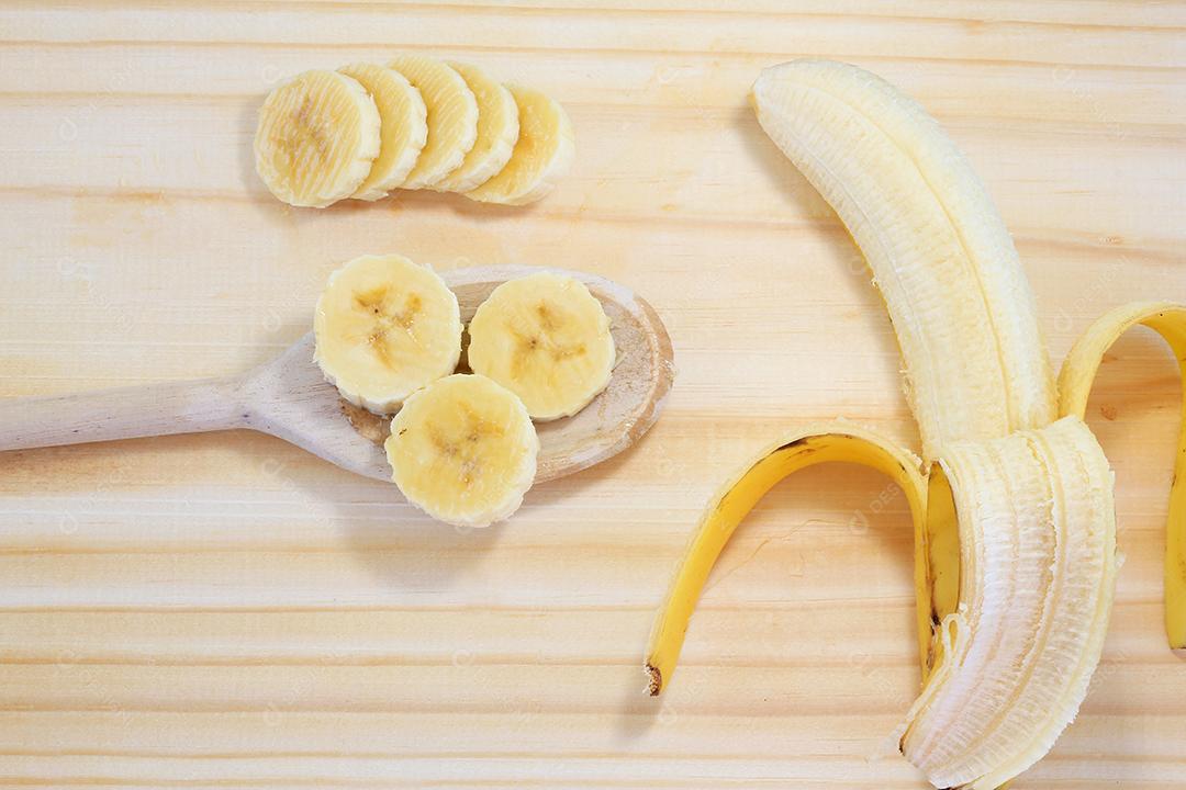 peeled banana on wood next to slices on wooden spoon, top view