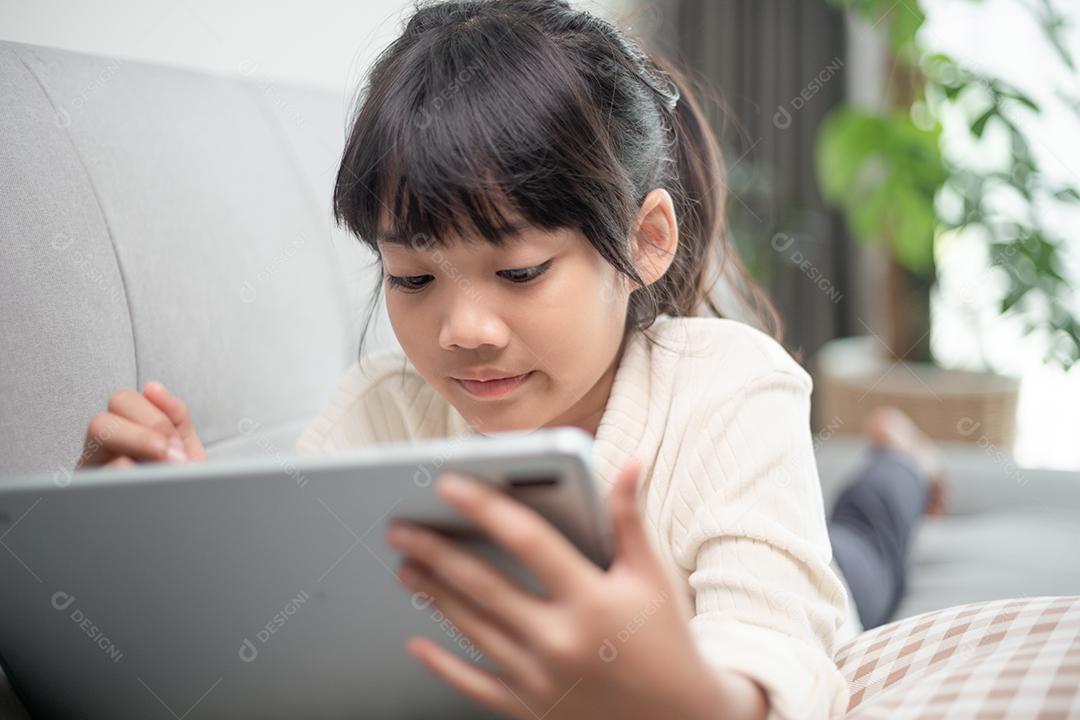 Menina sorridente, deitada no sofá confortável, desfrutando de jogar jogo  online no computador tablet digital viciada em tecnologia criança pequena  feliz usando aplicativos engraçados informações de navegação na web