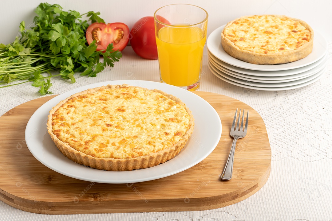 Torta quiche de queijo com ingredientes ao fundo e copo com suco