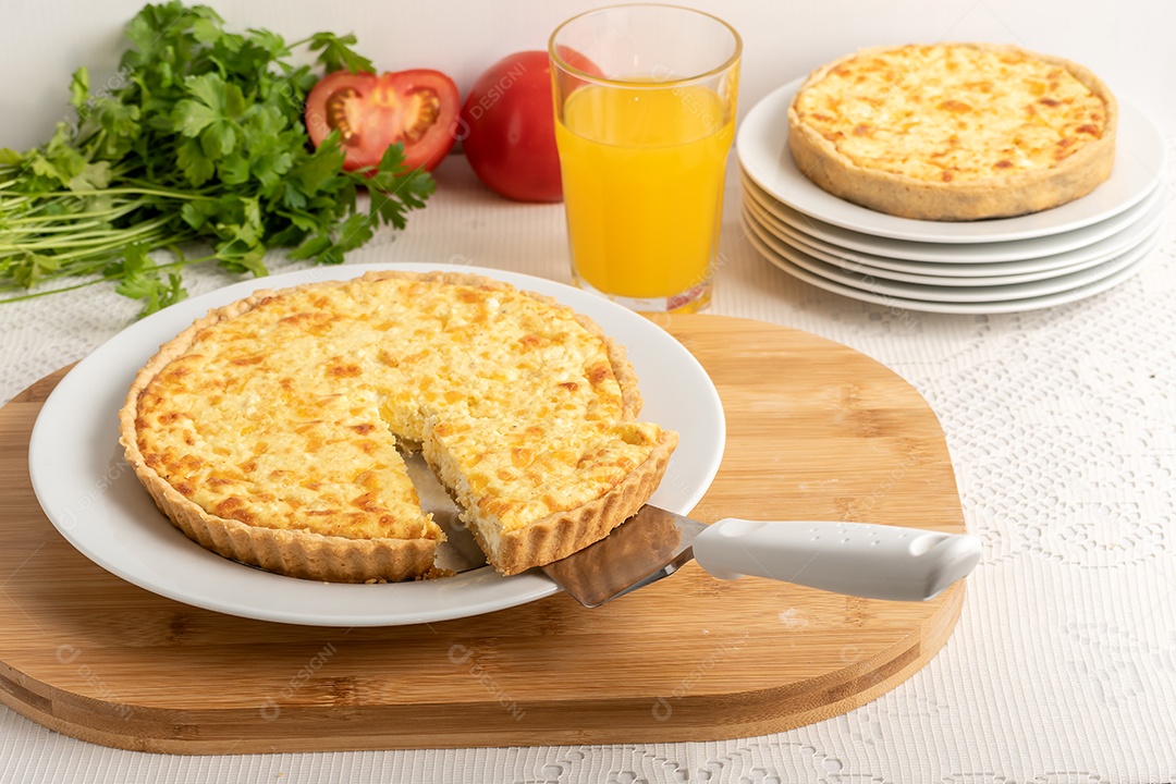 Torta quiche de queijo com ingredientes ao fundo e copo com suco